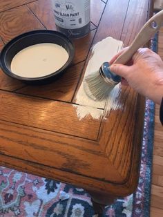 someone using a brush to paint the top of a wooden table with white paint on it