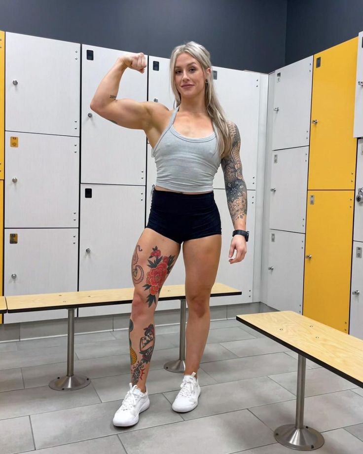 a woman posing in front of lockers with her arm and leg muscles raised up