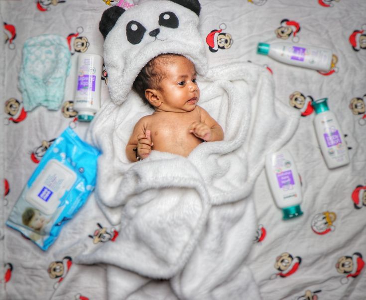 a baby wrapped up in a panda bear blanket surrounded by personal care products and toys