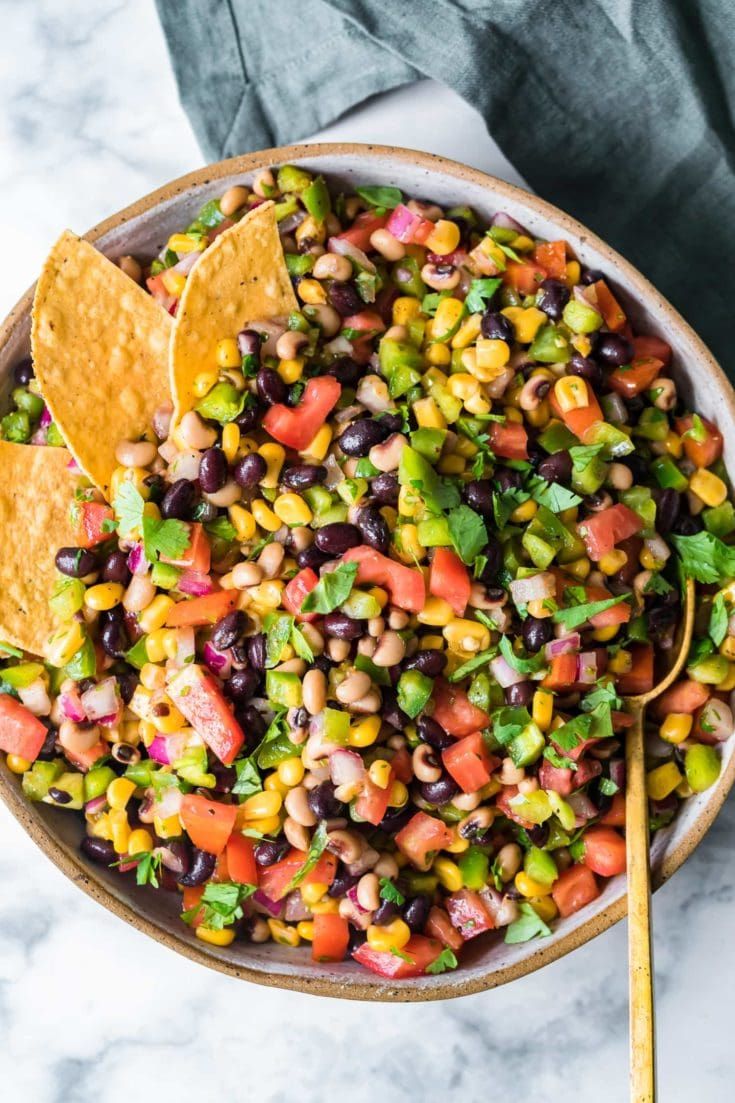 a bowl filled with black beans, corn and tortilla chips next to a wooden spoon