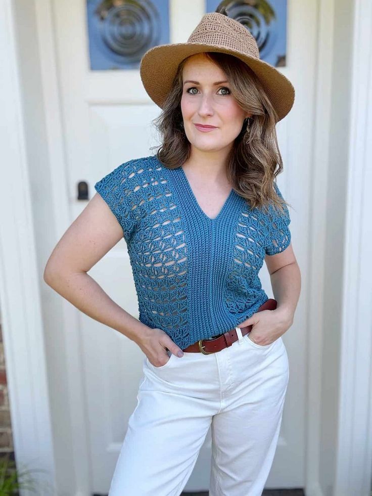 a woman standing in front of a door wearing white pants and a brown hat with her hands on her hips