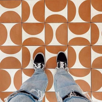 a person's feet with ripped jeans and sneakers on in front of a tiled floor