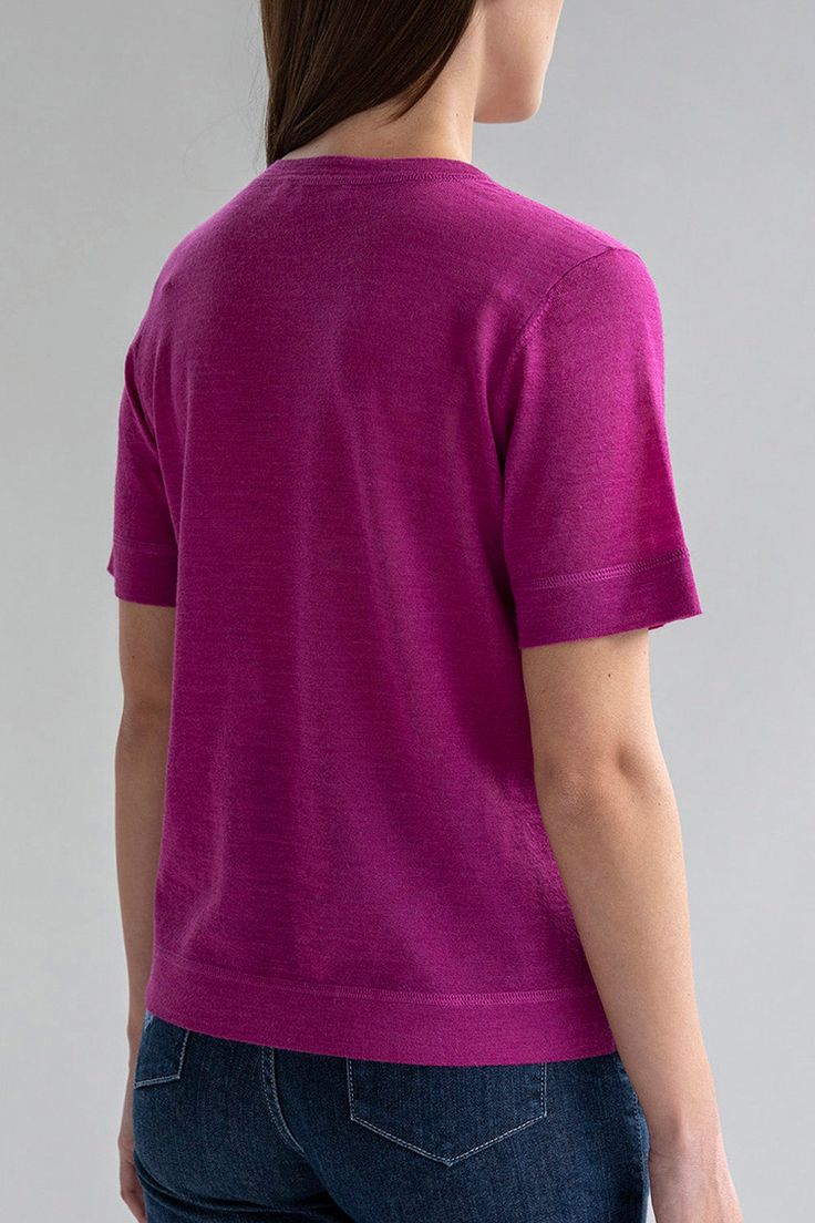 the back view of a woman wearing a bright pink shirt and jeans, with her hands in her pockets