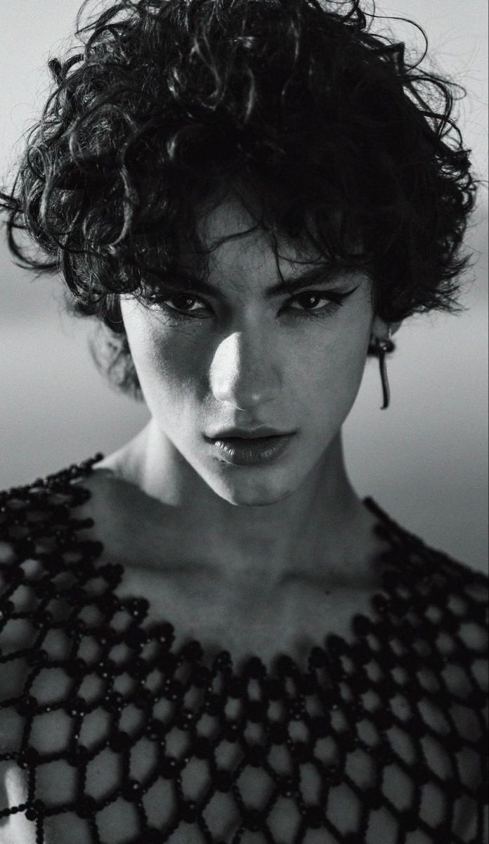 a black and white photo of a woman with curly hair, wearing a lacy top