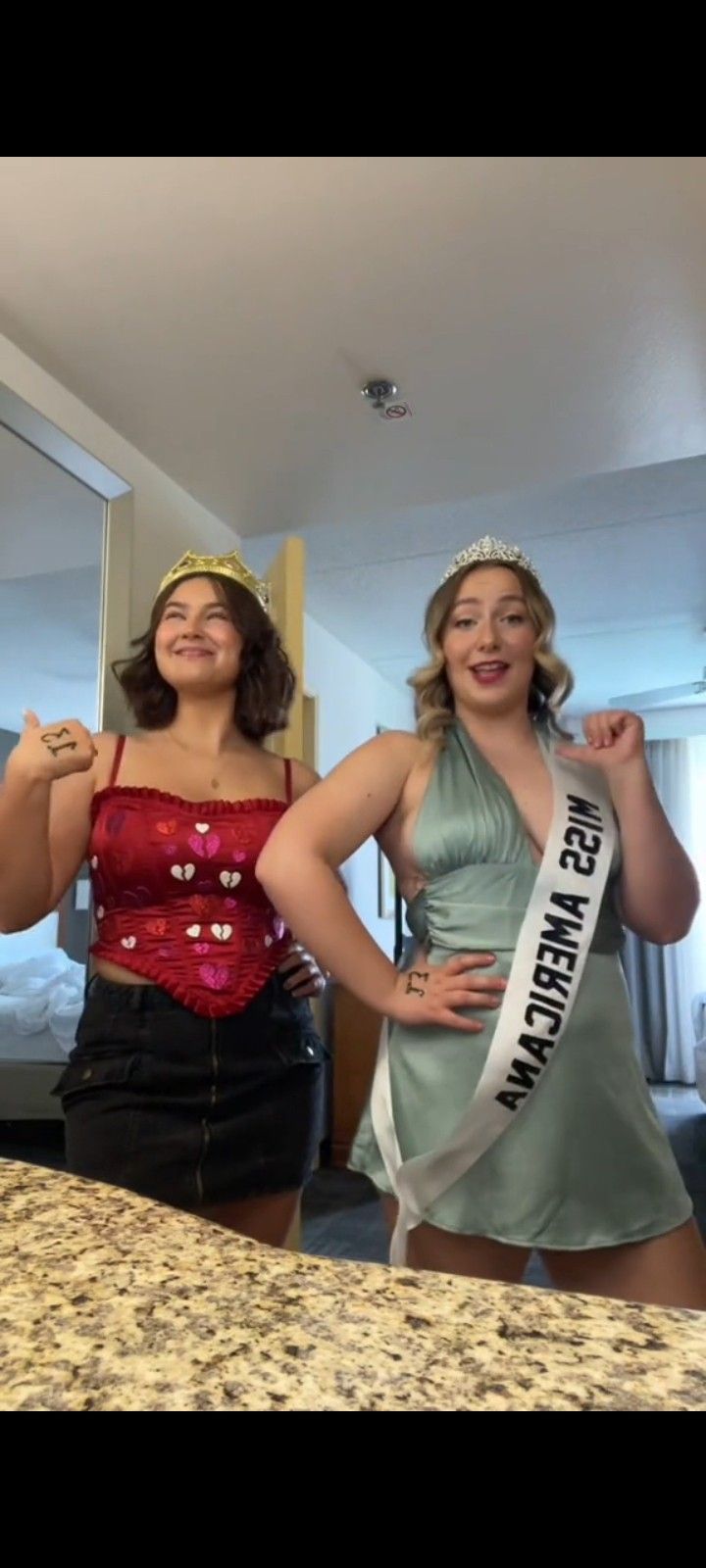 two women are standing in front of a mirror and one is wearing a tiara