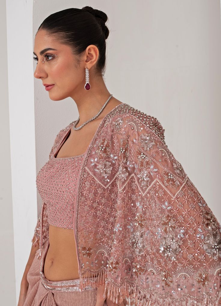 Elevate your style with the stunning Pastel Pink Draped Skirt with Embellished Cape, that effortlessly blends tradition with contemporary elegance. The pink cape features a sophisticated kimono sleeve , adorned with intricate florence embroidery using sequins, crystal tassels, cutdana, and bead highlights, adding a touch of opulence. Paired perfectly with a sequin jaal embellished blouse, it offers a dazzling appeal, making you the center of attention. Completed with a draped skirt, designed for a flattering silhouette, exudes grace and charm, ensuring comfort and sophistication in every movement. Ideal for, this ensemble is a timeless addition to your wardrobe, exuding both modernity and tradition in every detail. Composition : Cape - Organza ,Skirt - Platinoir Crepe Care: Dry Clean Only Cape Organza, Embroidered Cape, Pink Cape, Organza Skirt, Indian Wedding Wear, Embellished Blouse, Draped Skirt, Kimono Sleeve, Wedding Wear