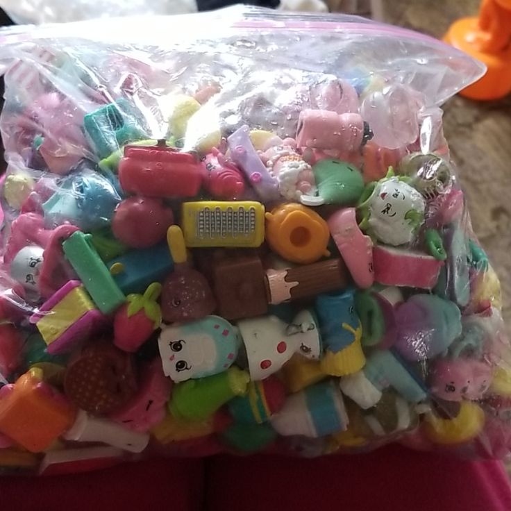 a plastic bag filled with lots of small toy animals and other toys on top of a person's lap