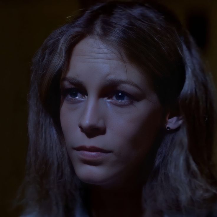 a woman with long hair and blue eyes stares into the distance in a dark room