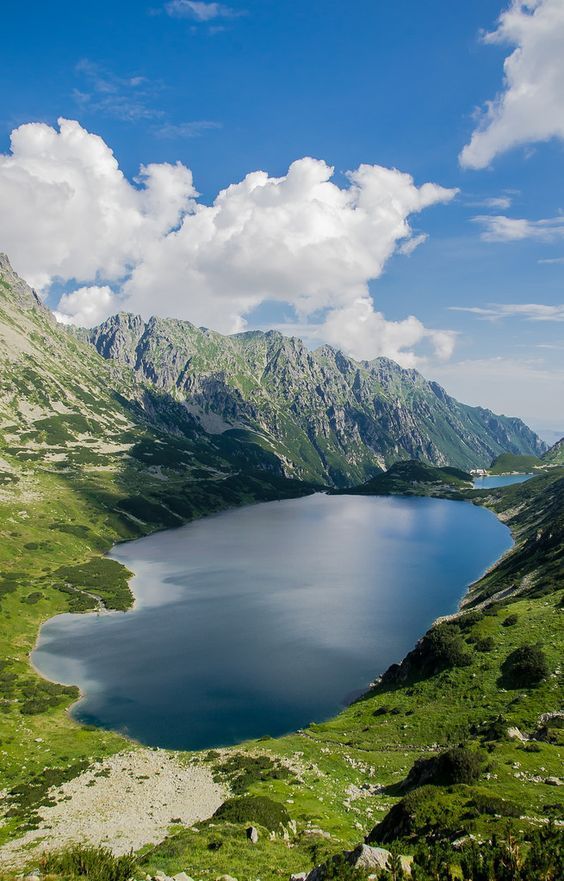 a large lake surrounded by mountains under a blue sky with white clouds in the distance