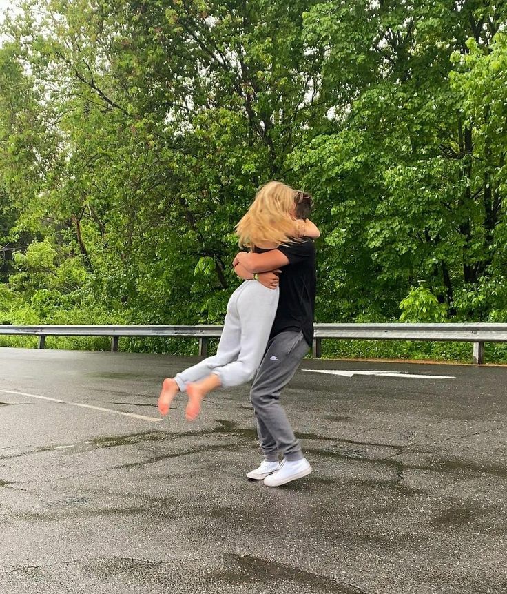 two people hugging in the middle of an empty parking lot with trees in the background