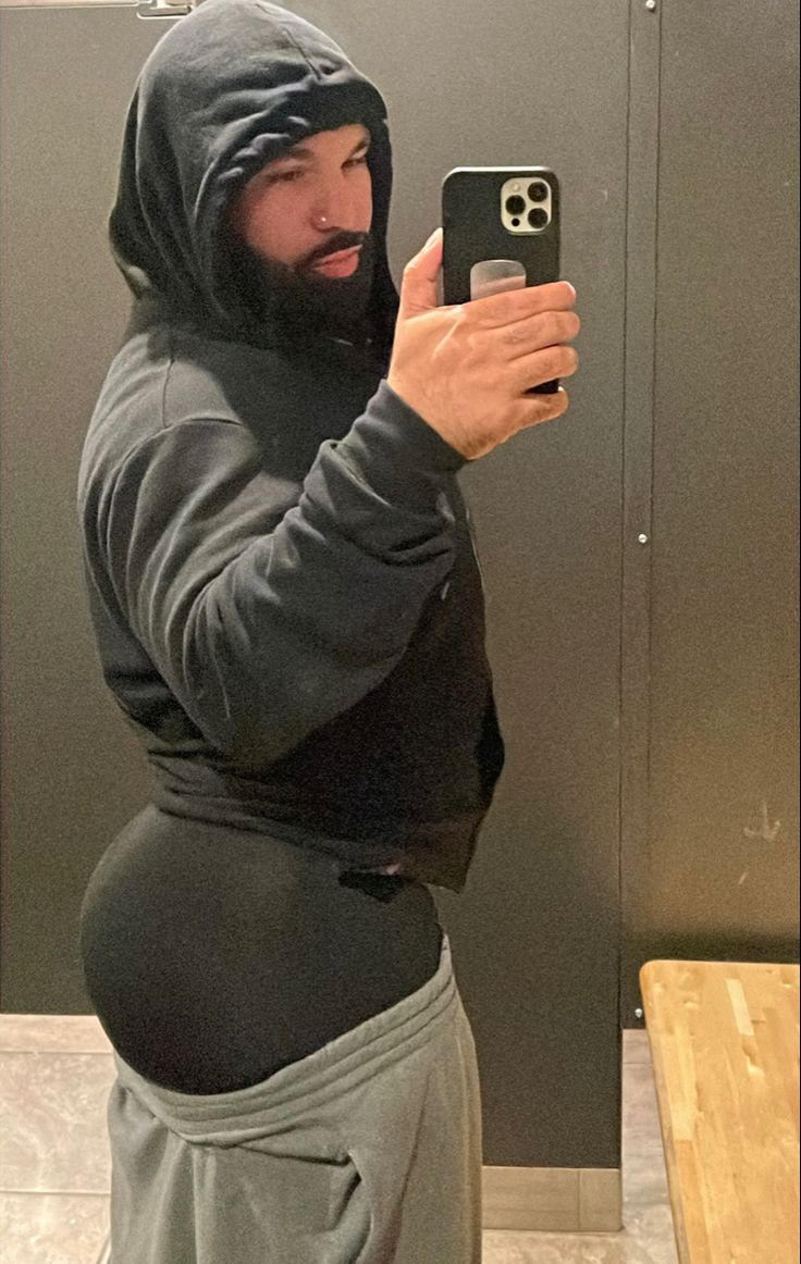 a man wearing a hoodie taking a selfie in front of a bathroom mirror