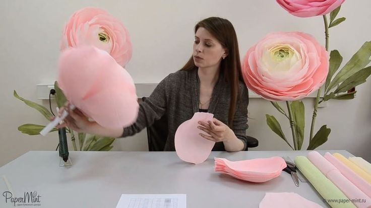 a woman sitting at a table with pink flowers in front of her and making a heart shaped lollipop