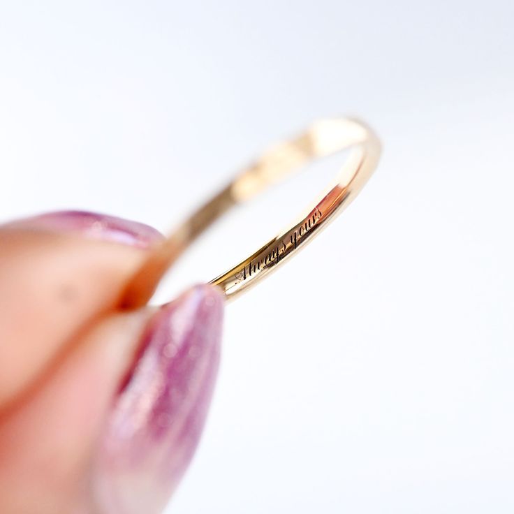 a close up of a person's hand holding a gold ring with writing on it