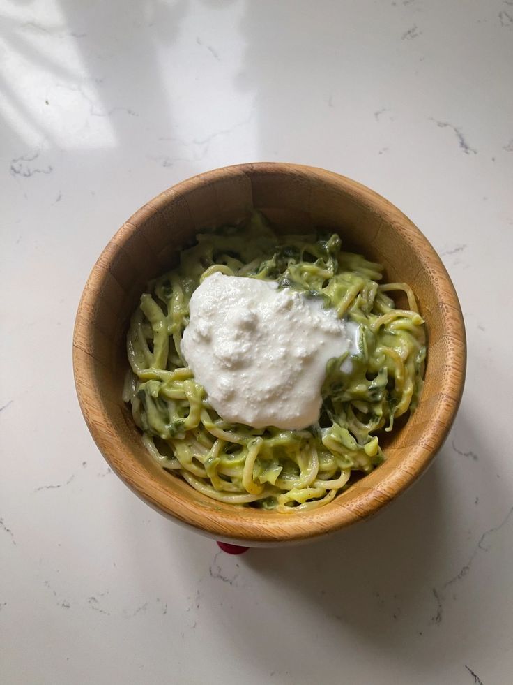 a wooden bowl filled with pasta and sour cream on top of a white countertop