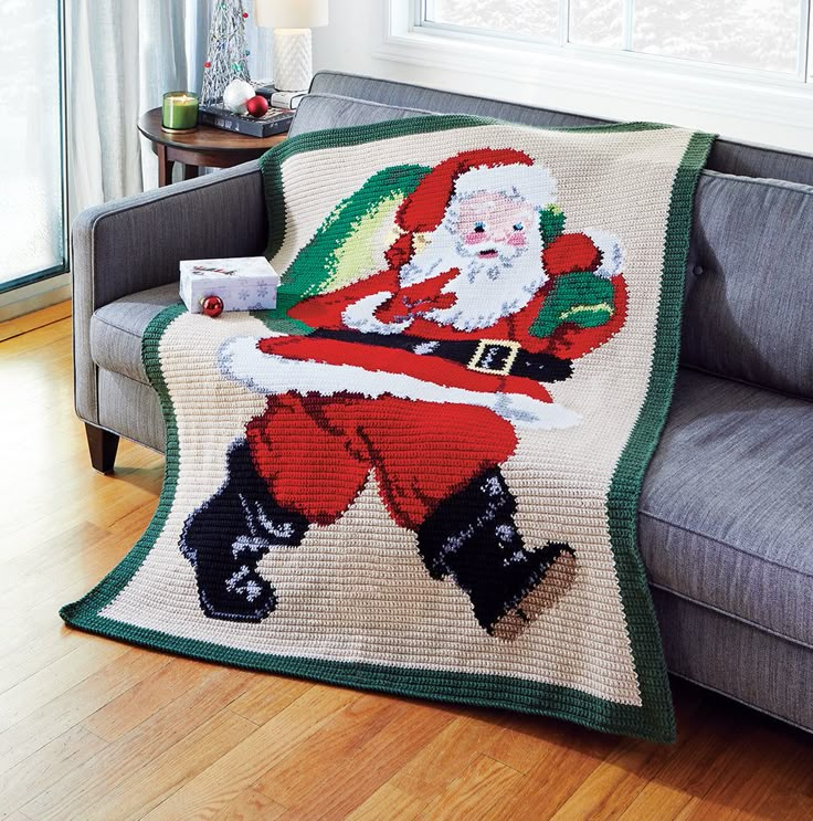 a crocheted santa clause blanket sitting on top of a couch next to a window