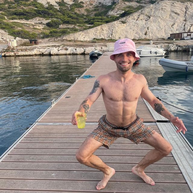 a shirtless man standing on a dock holding a yellow object in his right hand