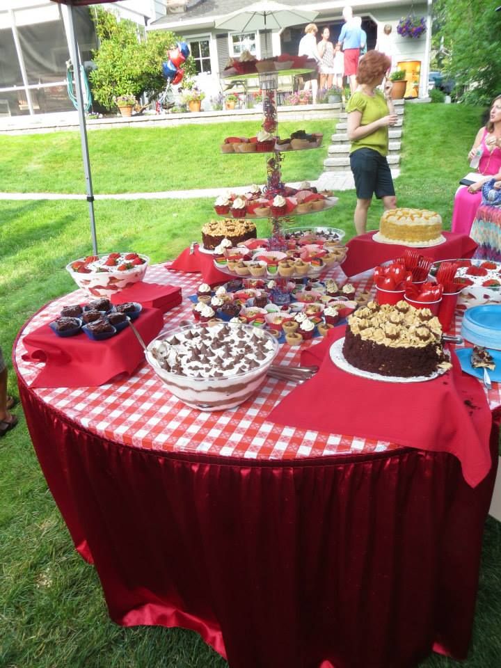 a table topped with lots of cakes and desserts on top of a red table cloth