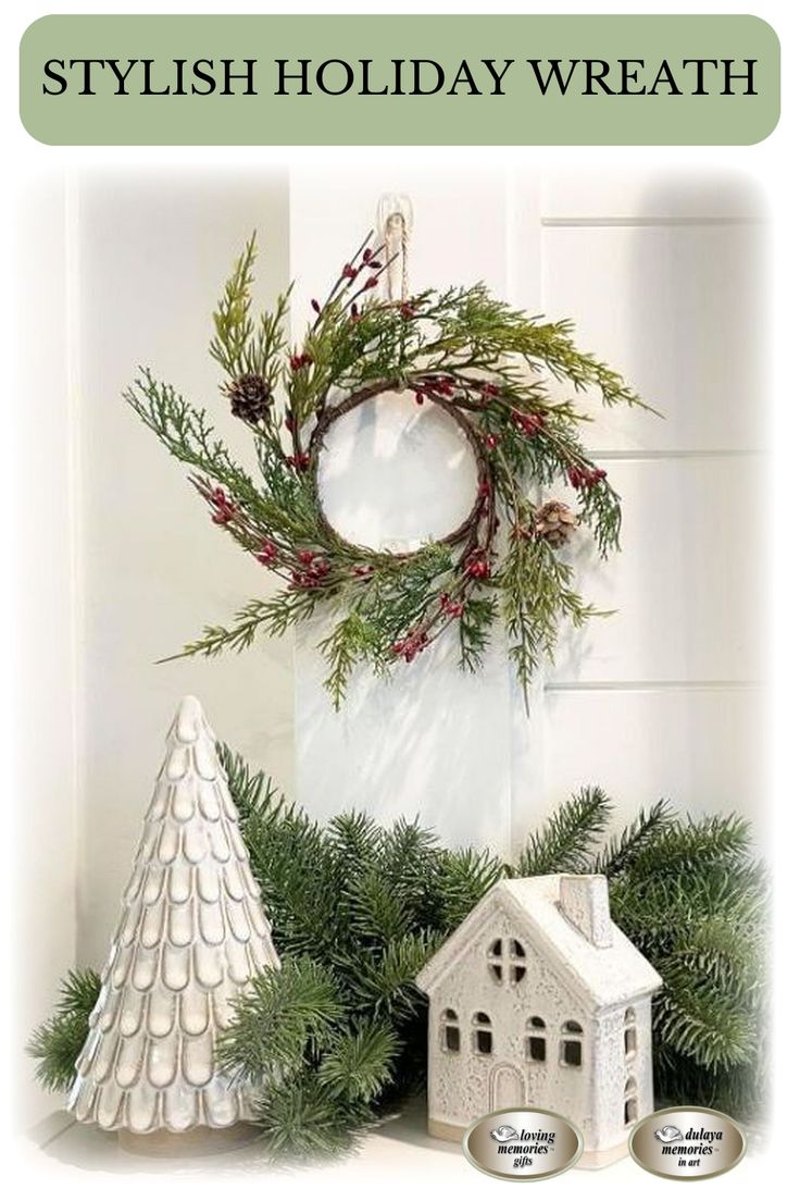 a white christmas wreath sitting on top of a mantle next to a small house and tree