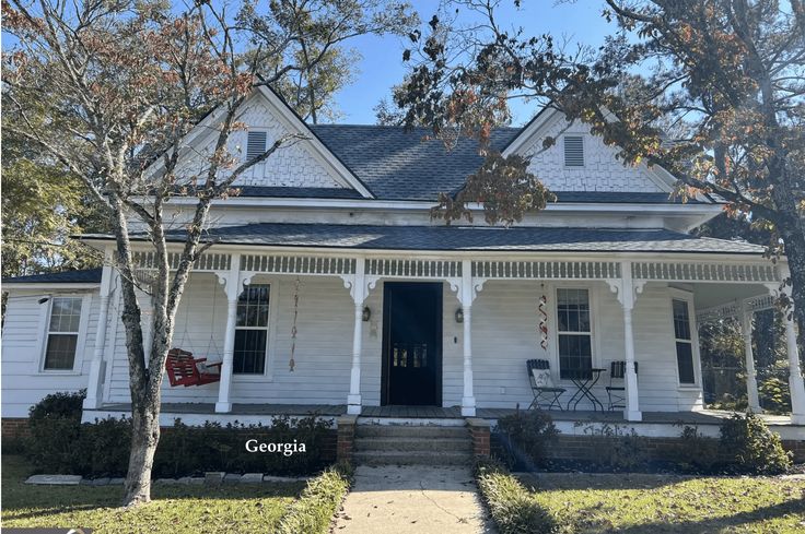 a white house with black shutters on the front porch and two flags hanging from it's roof