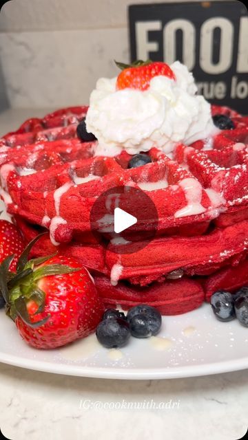 a white plate topped with waffles covered in blueberries and strawberries next to a pile of whipped cream