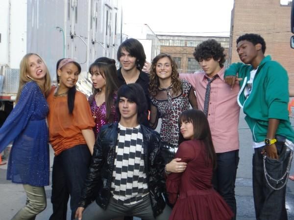 a group of young people standing next to each other on a city street with buildings in the background