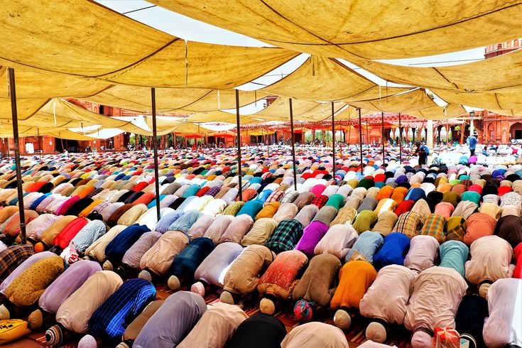 a large group of people sitting on the ground in front of tents covered with yellow tarps