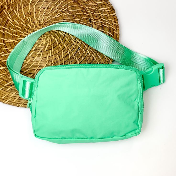 Pictured is a rectangle fanny pack with a top zipper with tassel in turquoise. This bag also includes a turquoise strap and turquoise accents. This bag is pictured on a white and brown patterned background. Green Crossbody Chest Bag For On-the-go, Green Belt Bag With Pockets For On-the-go, Green Nylon Belt Bag With Adjustable Strap, Versatile Green Chest Bag With Adjustable Strap, Trendy Green Travel Chest Bag, Versatile Green Chest Bag For Travel, Trendy Green Chest Bag For Travel, Green Travel Chest Bag With Zipper Pocket, Green Nylon Travel Belt Bag