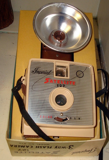 an old camera sitting in a box on top of a table next to a lamp