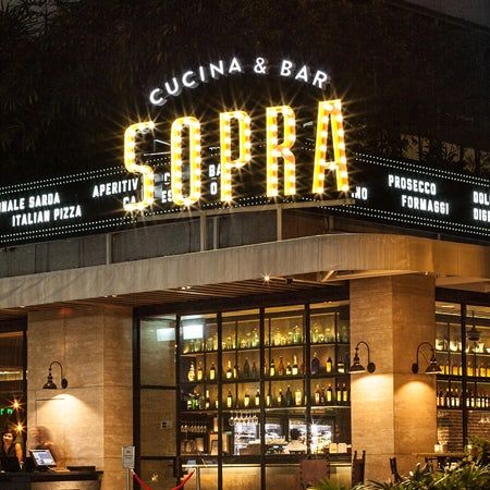 the entrance to an italian restaurant with lights on it's roof and people sitting at tables