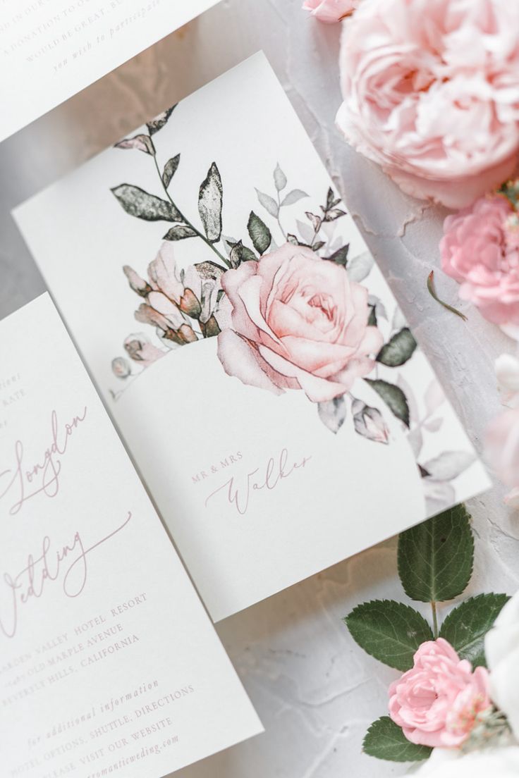 wedding stationery with pink flowers and greenery on the table next to each other