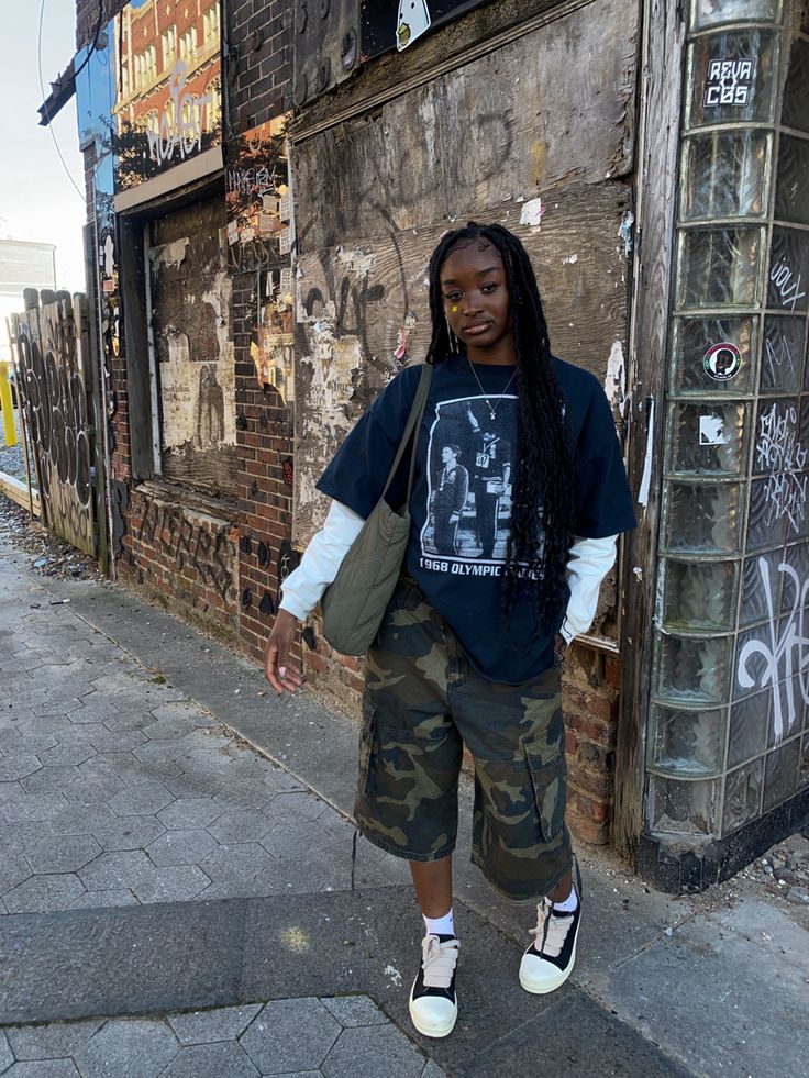 a woman standing in front of a building with graffiti on the walls and wearing camouflage shorts