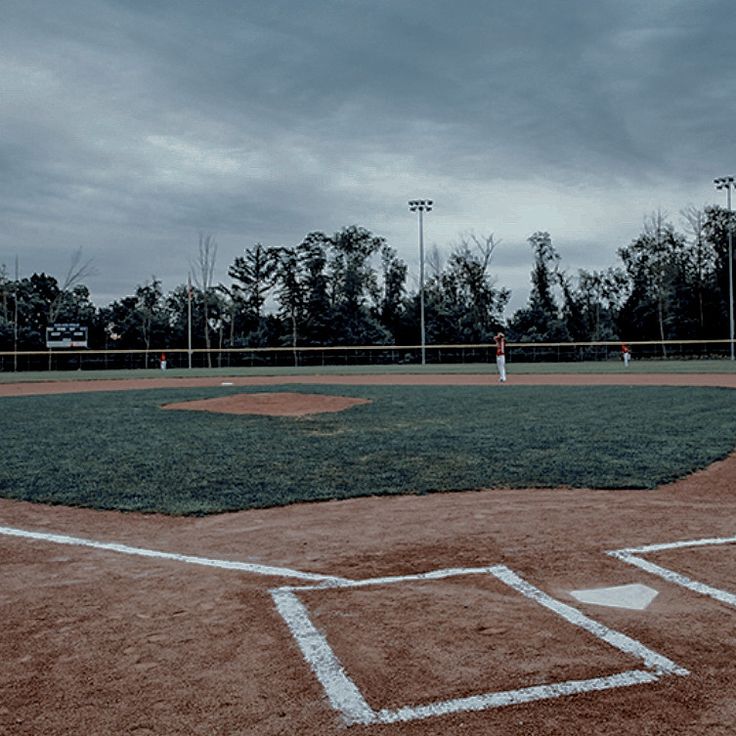 a baseball field with a batter, catcher and umpire in the outfield on a cloudy day