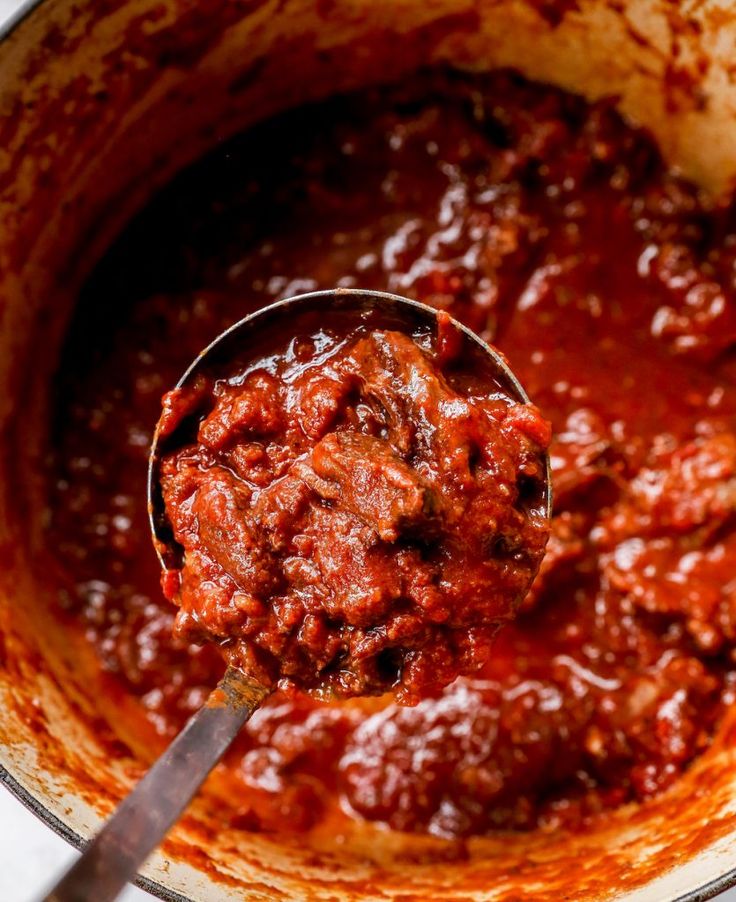 a ladle full of chili sauce being stirred with a wooden spoon in a pot