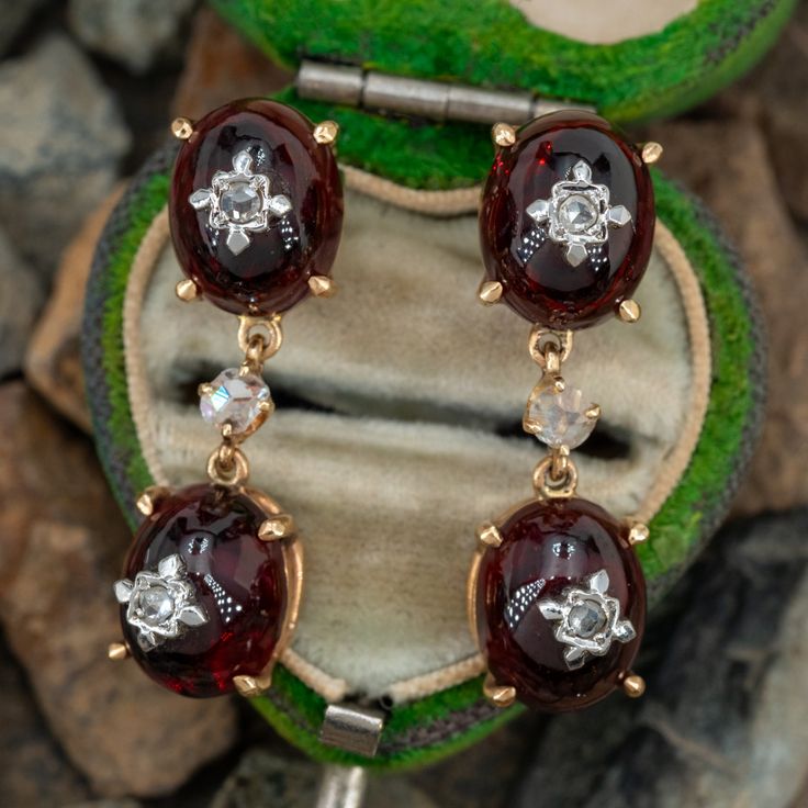 These beautiful dangle earrings are each accented with two (2) prong set, oval cabochon cut natural almandine garnet each topped with one (1) rose cut diamond bead set into a white gold setting. The diamond and garnet links are connected with a four-prong setting accented with one (1) rose cut diamond. The earrings measure 28mm X 8.2mm and are finished with friction style backs for pierced ears. Victorian Oval Earrings For Anniversary, Victorian Jewelry With Oval Matching Earrings, Fine Jewelry With Oval Jeweled Details, Fine Jewelry With Jeweled Oval Details, Oval Jeweled Fine Jewelry, Victorian Jewelry With Rose Cut Diamonds In Oval Shape, Elegant Garnet Oval Cabochon Jewelry, Elegant Jewelry With Oval Cabochon Garnet, Antique Jewelry With Gemstone Accents For Formal Occasions