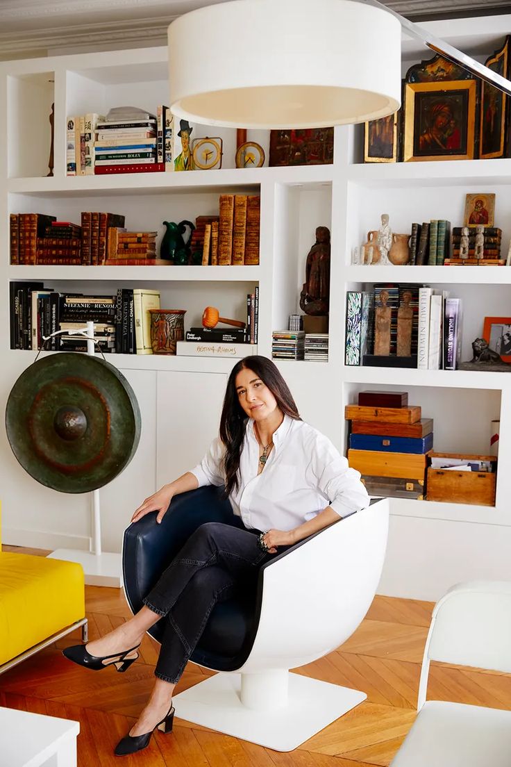 a woman is sitting on a chair in a room with bookshelves and shelves