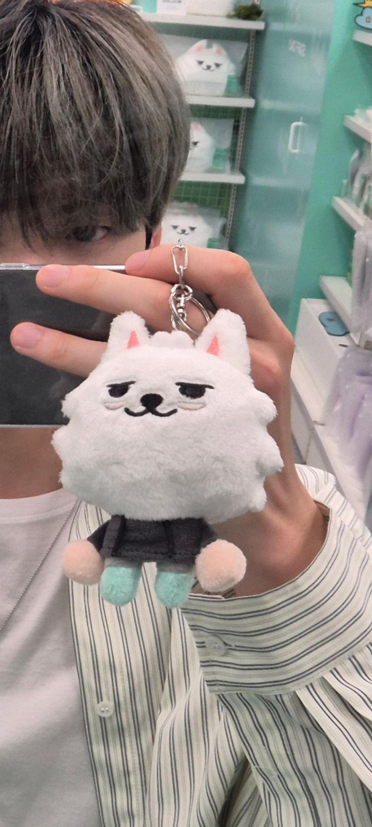 a person taking a selfie with a cell phone in front of them and a cat keychain hanging from the back