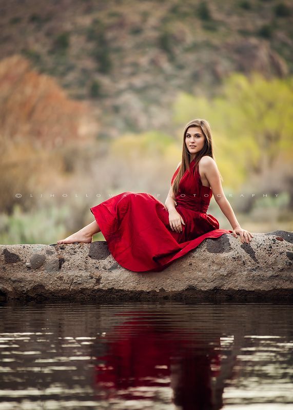 a woman in a red dress is sitting on a rock by the water