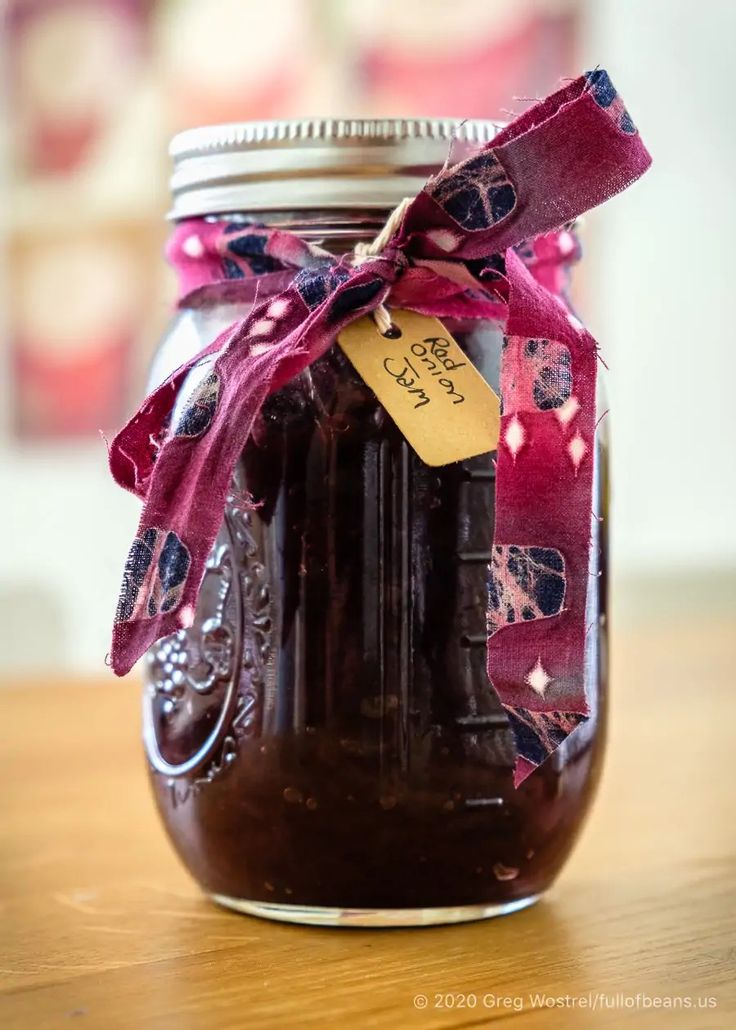 a glass jar filled with jam sitting on top of a wooden table next to a red ribbon