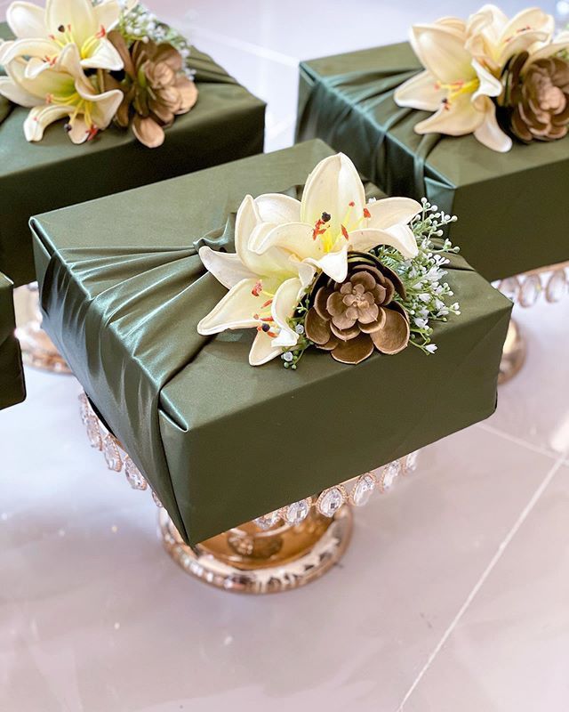 four green boxes with flowers on them sitting on top of a white tableclothed floor