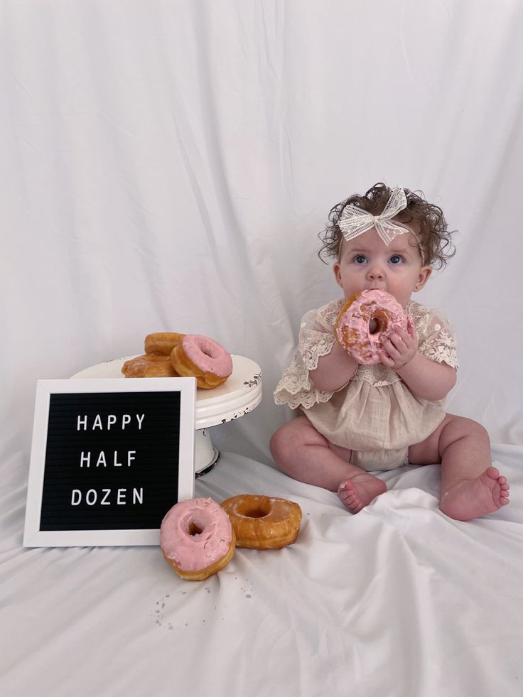 a baby sitting on the floor with doughnuts in front of her and a sign that says happy half dozen