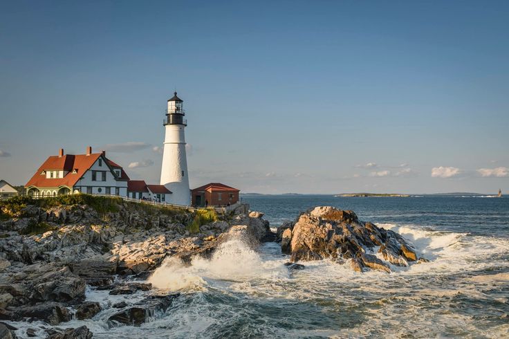 a light house sitting on top of a rocky cliff next to the ocean with waves crashing in front of it