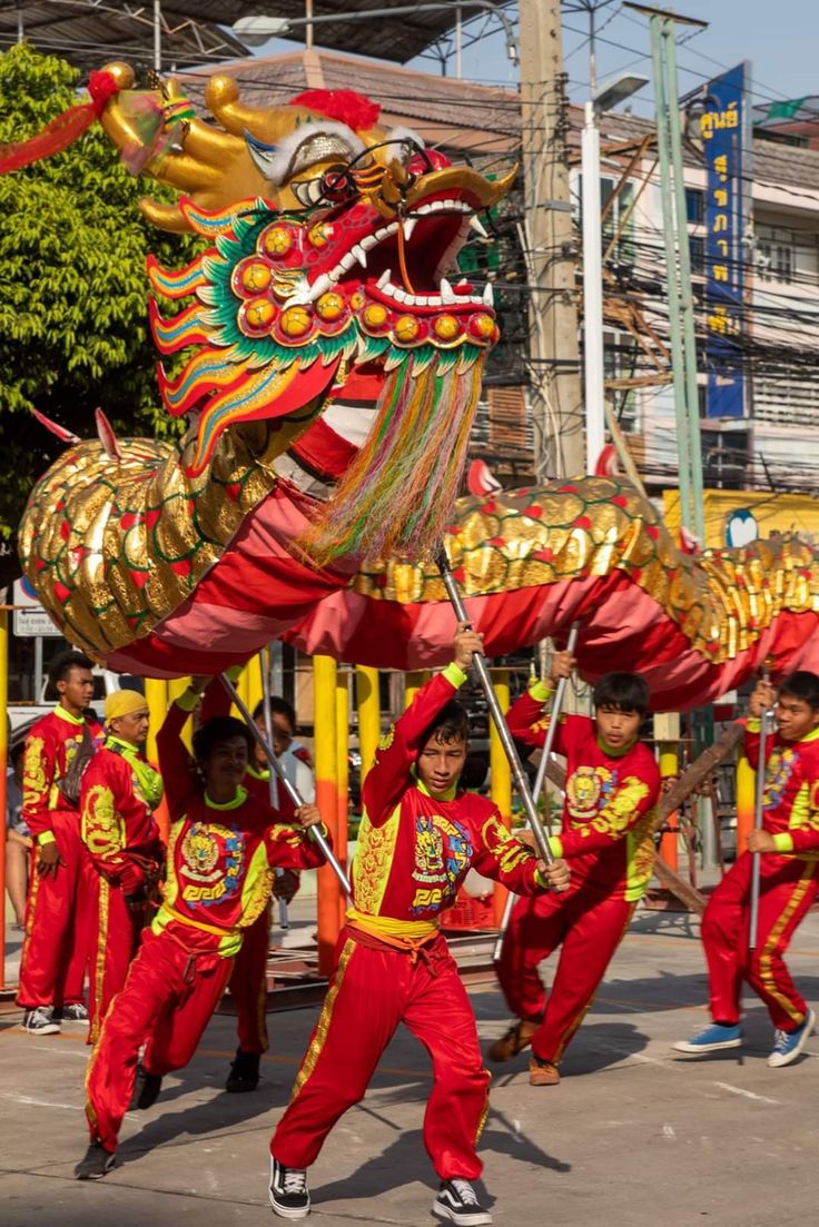 children in red and yellow costumes are performing on the street with a dragon shaped object