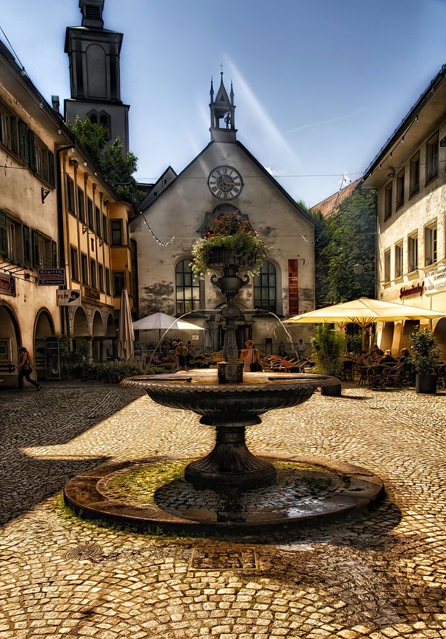 a fountain in the middle of a courtyard with tables and umbrellas