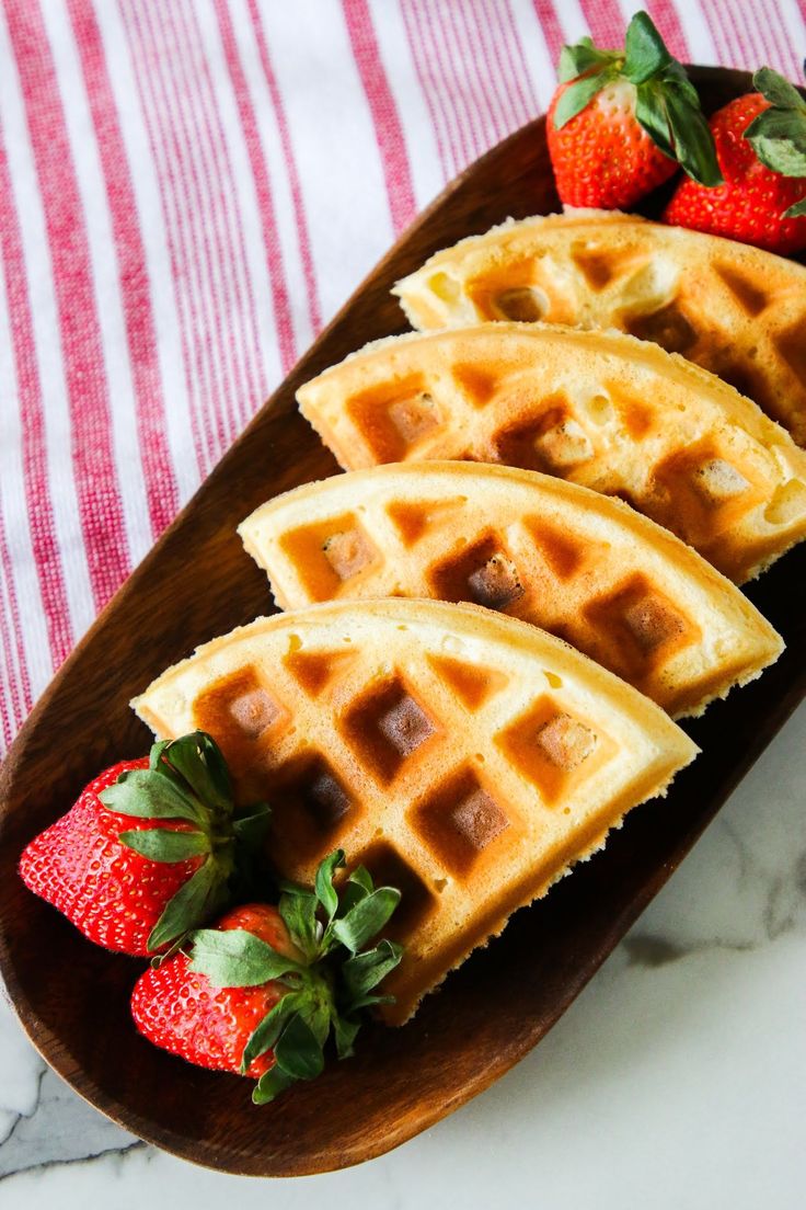 three waffles on a plate with strawberries next to it and a striped table cloth