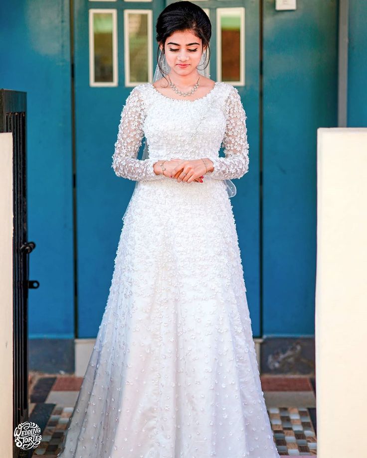 a woman standing in front of a blue door wearing a white wedding dress with long sleeves