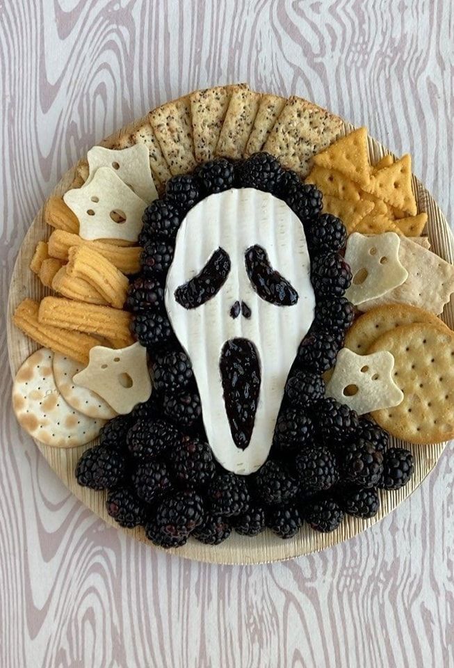 a plate with crackers and blackberries in the shape of a scream face