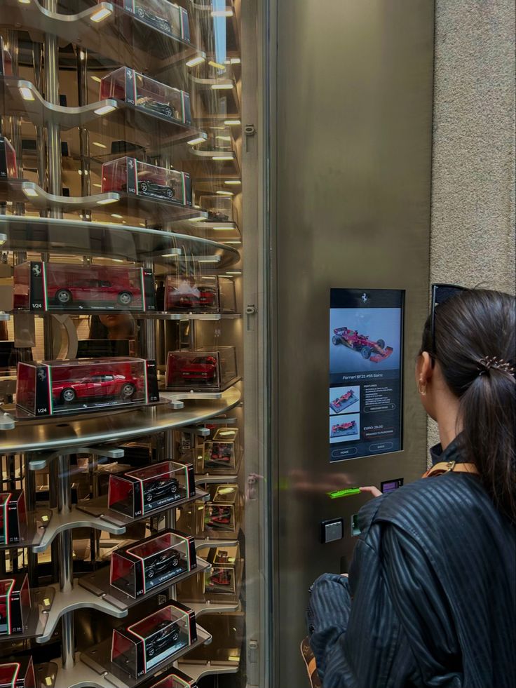 a woman standing in front of a display case with cars on the wall behind it