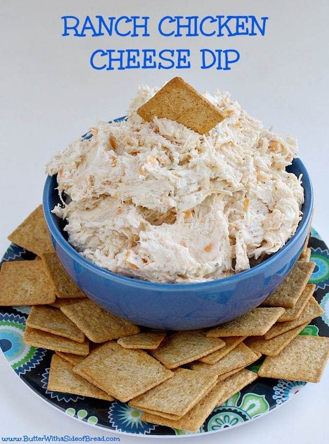 a blue bowl filled with chicken cheese dip surrounded by crackers on a colorful plate