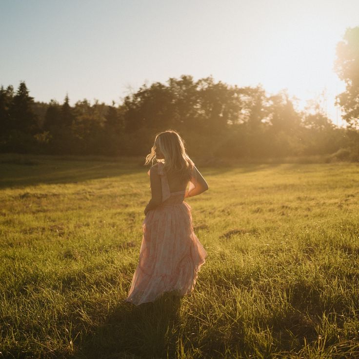 a woman in a long dress is standing in the grass with her back to the camera