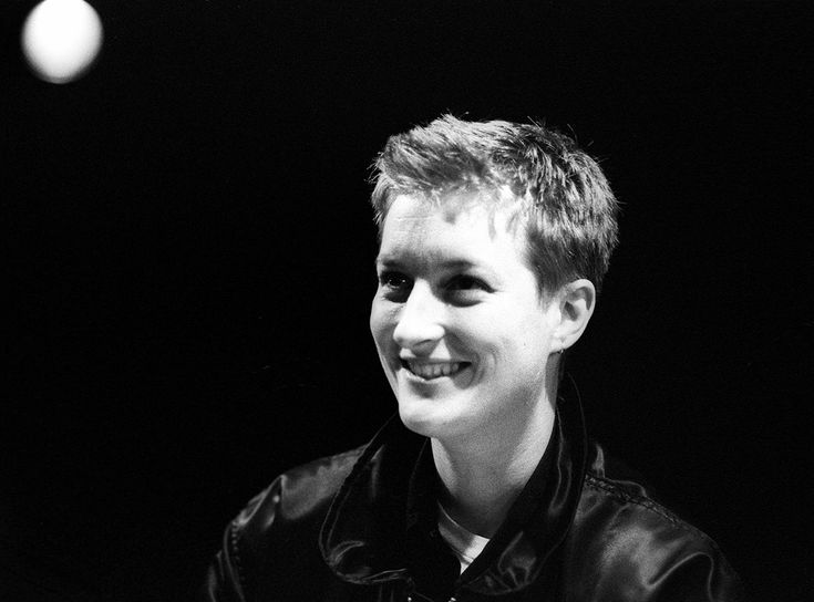 black and white photograph of a young man in leather jacket smiling at the camera with two balls behind him